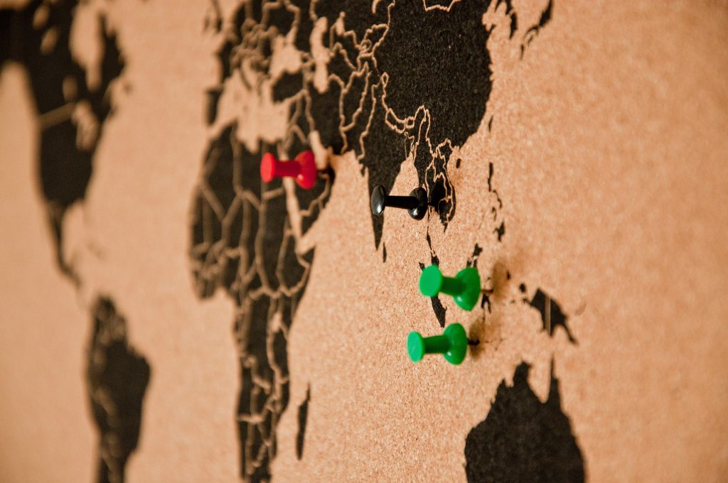 Thumbtacks stuck in places of the world on a corkboard